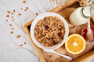 Eine Schale Müsli und frische Milch sowie eine Orange zeigen, wie einfach Ernährung gegen Erkältung sein kann!