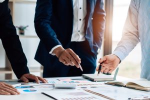 Eine Gruppe von Menschen steht über einem Tisch mit Plänen als Sinnbild für Stressmanagement Training